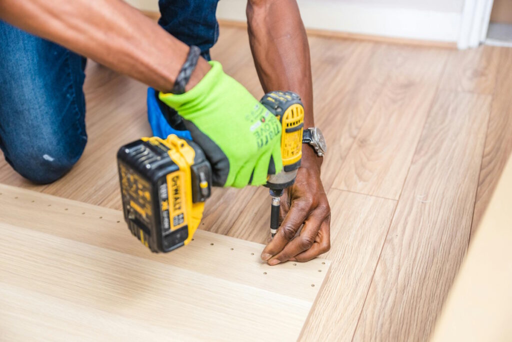 Person holding a DeWalt cordless hand drill while installing flooring, demonstrating DIY home renovation and flooring installation process.